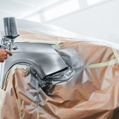 Painting job in progress. Caucasian automobile repairman in uniform works in garage.